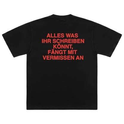 Rückseite eines schwarzen T-Shirts mit einem zentrierten, roten Aufdruck in Großbuchstaben: „ALLES WAS IHR SCHREIBEN KÖNNT, FÄNGT MIT VERMISSEN AN“.